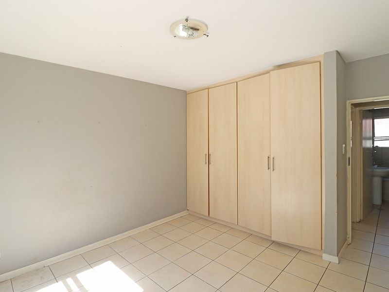 An empty bedroom featuring neutral tiled flooring, built-in wooden cupboards, and a view into the adjacent bathroom.
