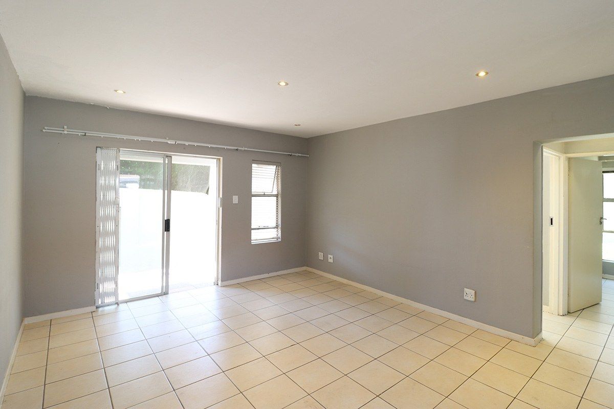 An empty, neutrally painted living room featuring tiled flooring, recessed downlights, and a sliding glass door providing access to the exterior.