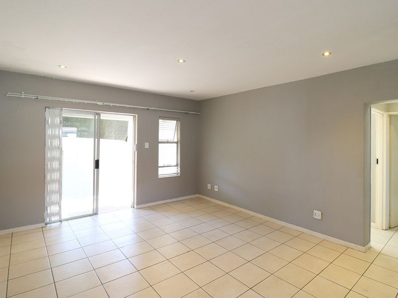An empty, neutrally painted living room featuring tiled flooring, recessed downlights, and a sliding glass door providing access to the exterior.