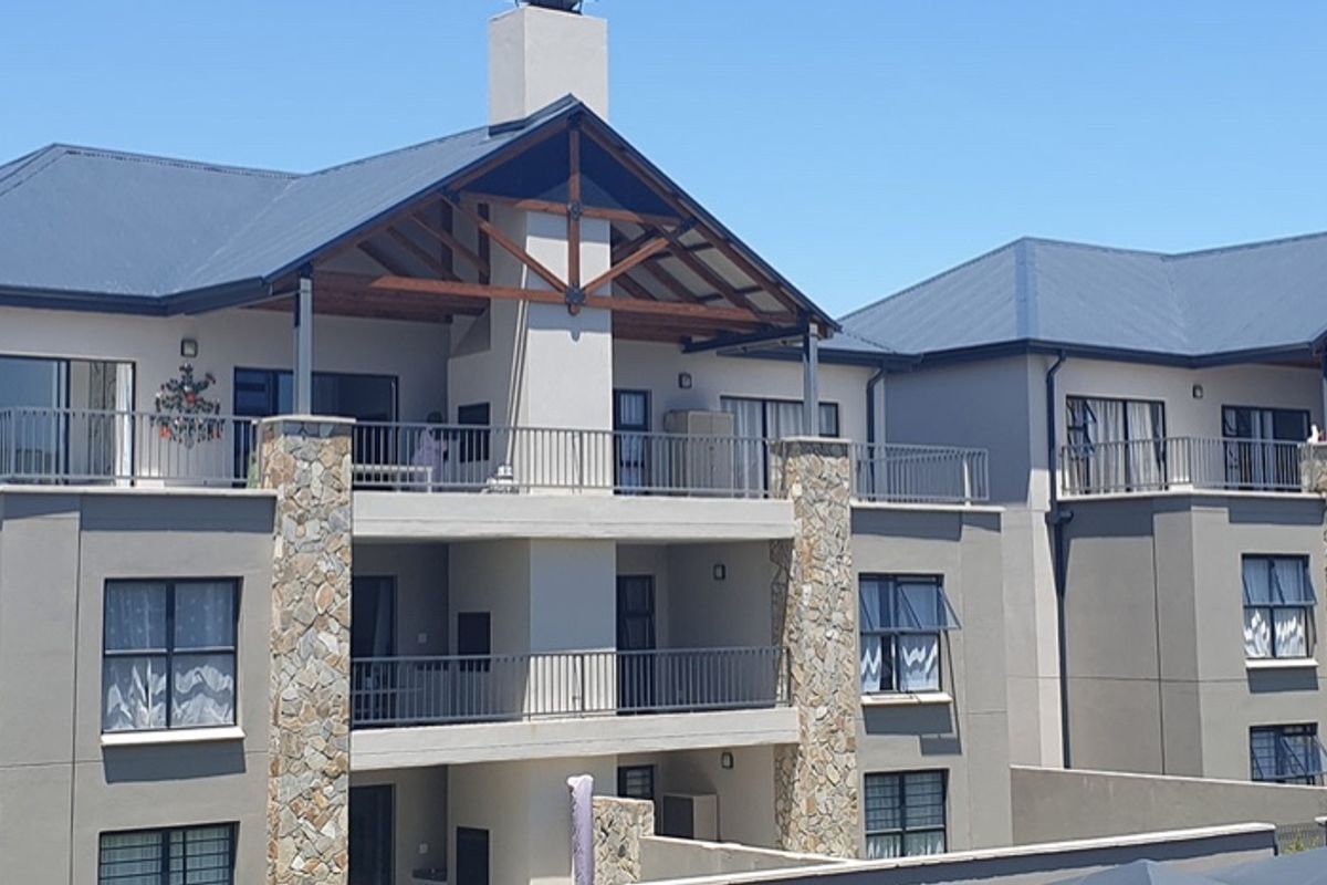 Rear elevation of a multi-story apartment complex featuring stone-clad pillars, metal roof, and private balconies with metal railings.
