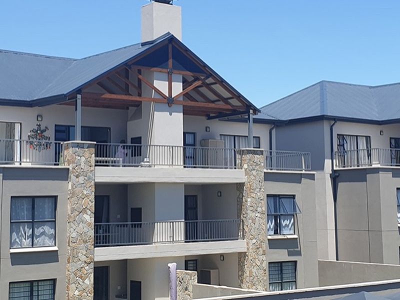 Rear elevation of a multi-story apartment complex featuring stone-clad pillars, metal roof, and private balconies with metal railings.