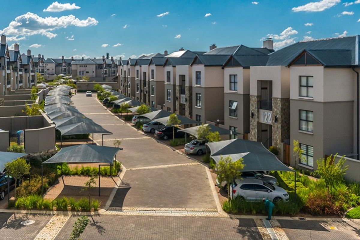 Aerial view of a modern apartment complex featuring paved driveways, designated shade cloth parking bays, and well-maintained multi-story residential buildings.