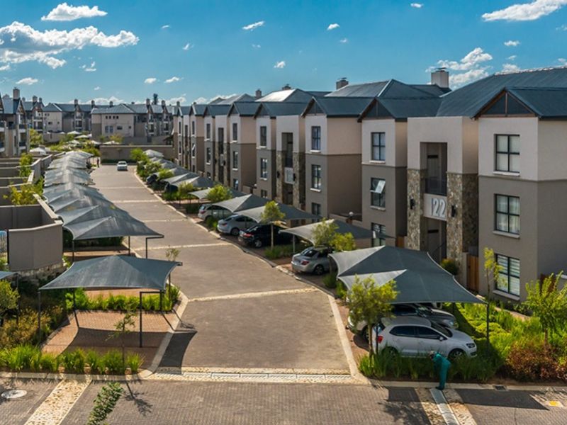 Aerial view of a modern apartment complex featuring paved driveways, designated shade cloth parking bays, and well-maintained multi-story residential buildings.