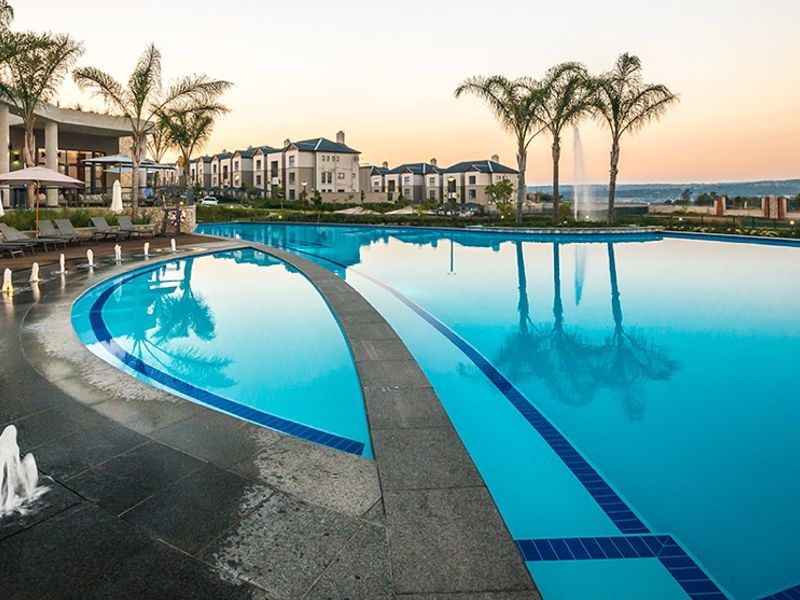 A well-maintained communal swimming pool area featuring water fountains, stone paving, and a covered patio area within a residential estate.