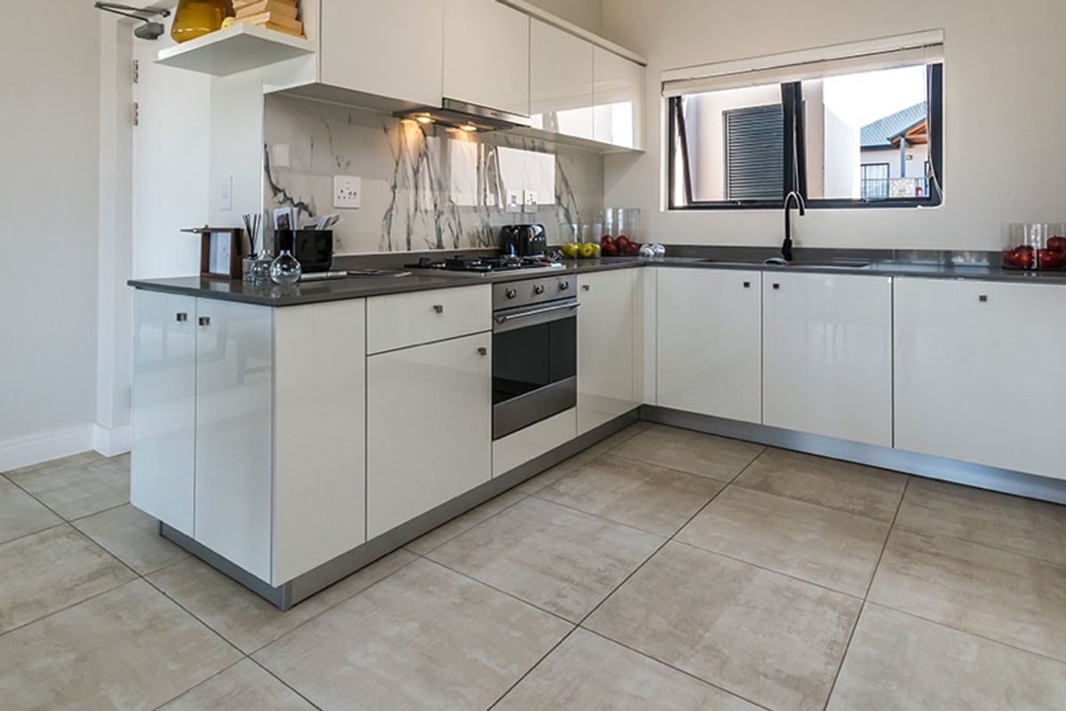 Modern kitchen featuring glossy white cabinetry, stone countertops, marble-look splashback, built-in oven, gas hob, and tiled flooring.