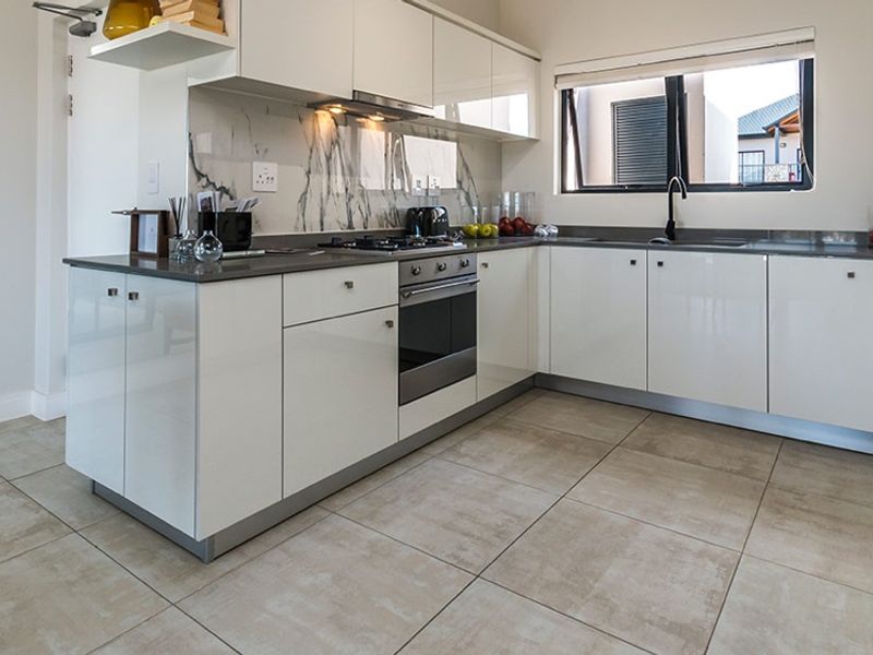 Modern kitchen featuring glossy white cabinetry, stone countertops, marble-look splashback, built-in oven, gas hob, and tiled flooring.