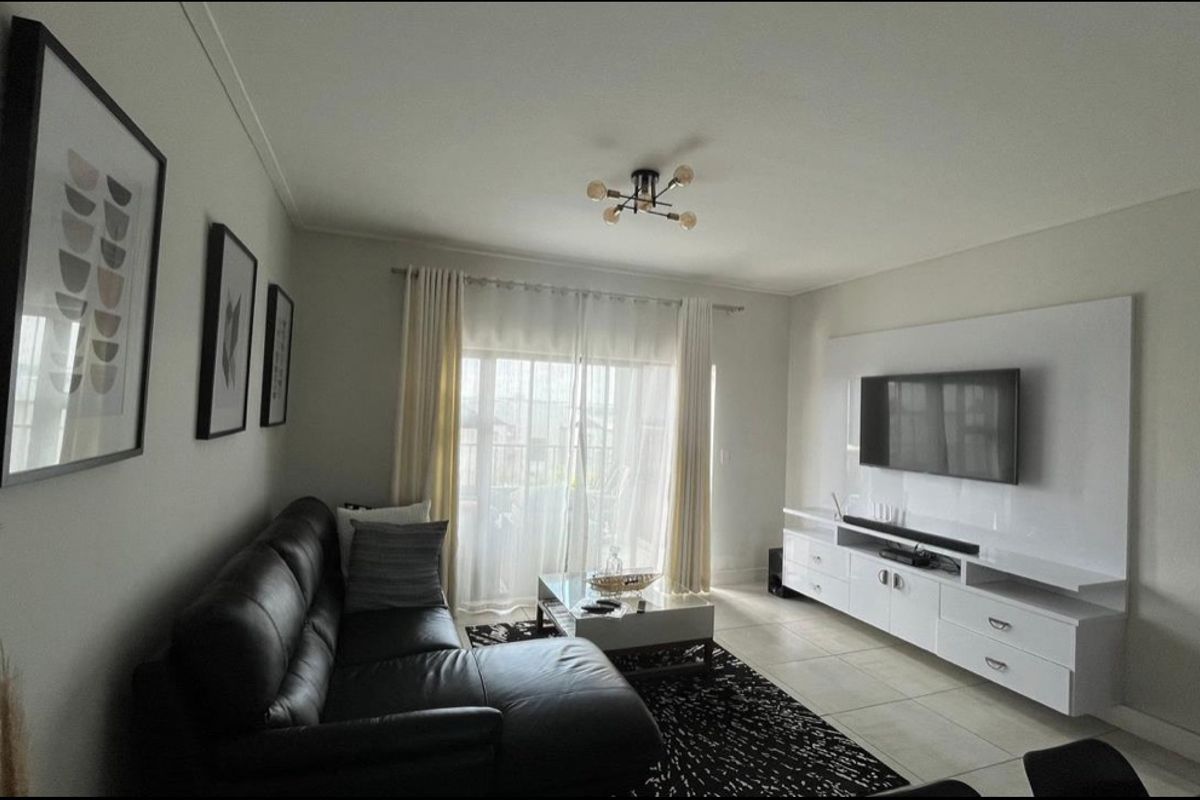 A well-maintained living room featuring tiled flooring, a built-in media console, and a sliding glass door providing access to the outdoor area.