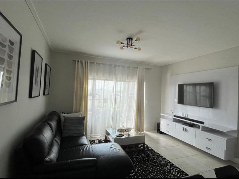 A well-maintained living room featuring tiled flooring, a built-in media console, and a sliding glass door providing access to the outdoor area.