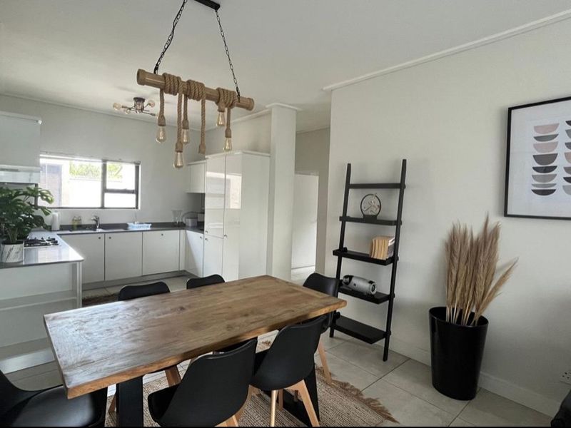 Modern open-plan kitchen and dining area featuring sleek white cabinetry, integrated appliances, tiled flooring, and contemporary pendant lighting.