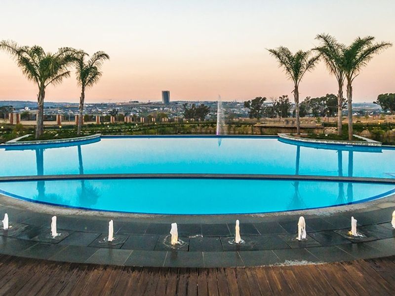A well-maintained infinity pool featuring integrated water fountains, surrounded by timber decking and offering expansive views of the surrounding landscape.