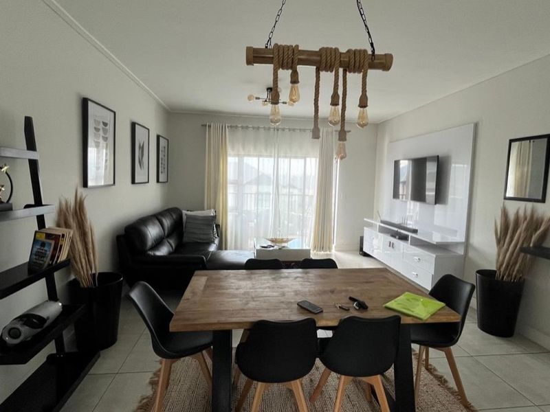 An open-plan living and dining area featuring tiled floors, a built-in media unit, and access to a balcony through sliding glass doors.