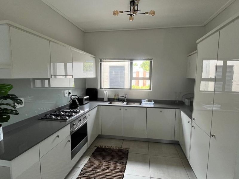 Modern kitchen featuring sleek white cabinetry, stone countertops, a gas hob, built-in oven, and a glass splashback with ample storage space.