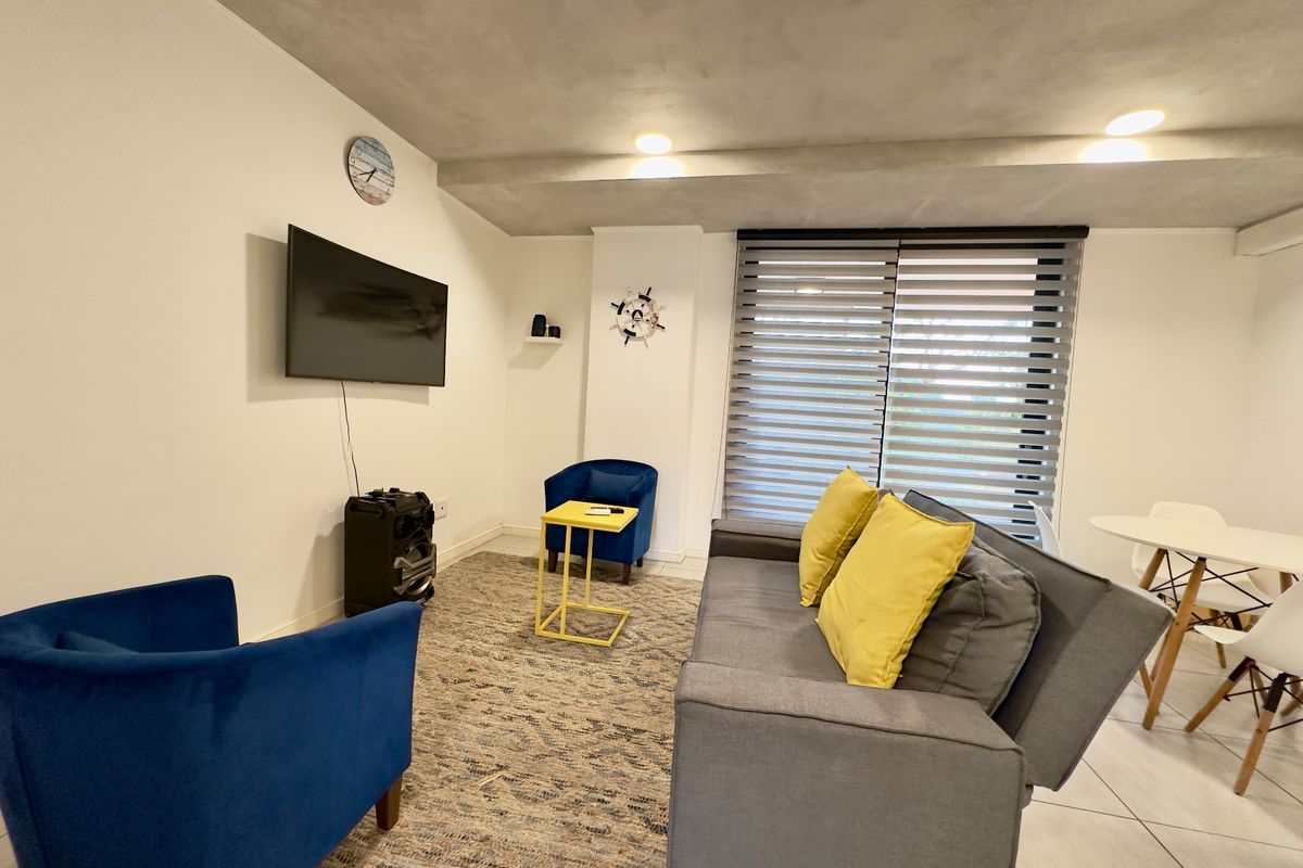 A living room area featuring tiled flooring, recessed ceiling lighting, and modern roller blinds, providing a functional space for relaxation.