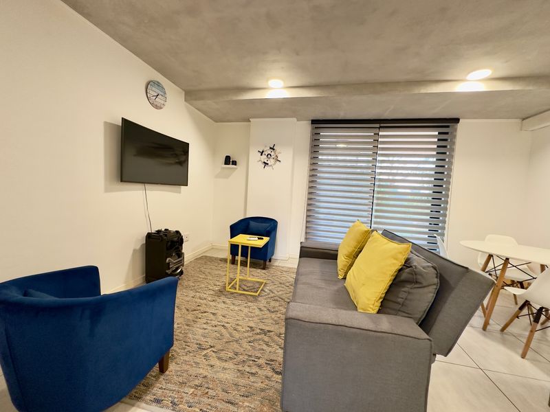 A living room area featuring tiled flooring, recessed ceiling lighting, and modern roller blinds, providing a functional space for relaxation.