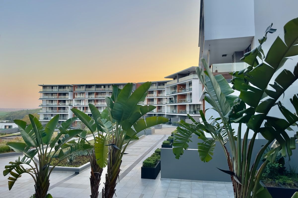 A modern apartment complex featuring a well-maintained paved courtyard, landscaped planters, and multiple levels of private balconies at sunset.
