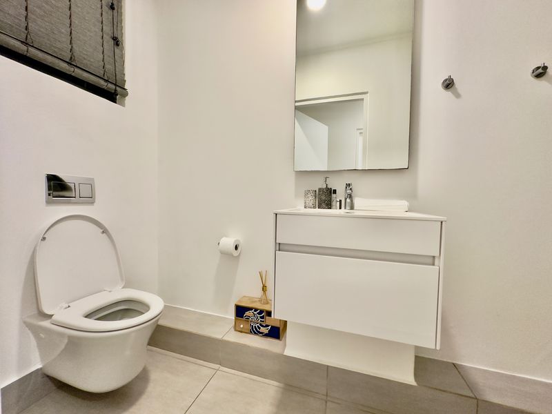 A modern, clean bathroom featuring a wall-mounted toilet with a concealed cistern, a sleek vanity cabinet with a basin, and a wall-mounted mirror.