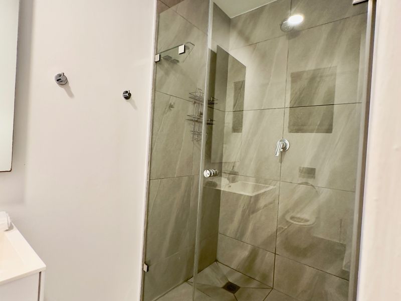 Modern bathroom featuring a glass-enclosed walk-in shower with large-format grey tiles and a sleek vanity unit.