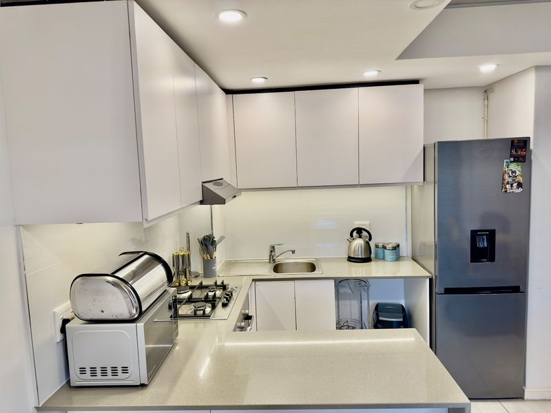 Modern kitchen featuring white cabinetry, stone countertops, a gas hob with extractor fan, and a glass splashback, offering a clean and functional workspace.