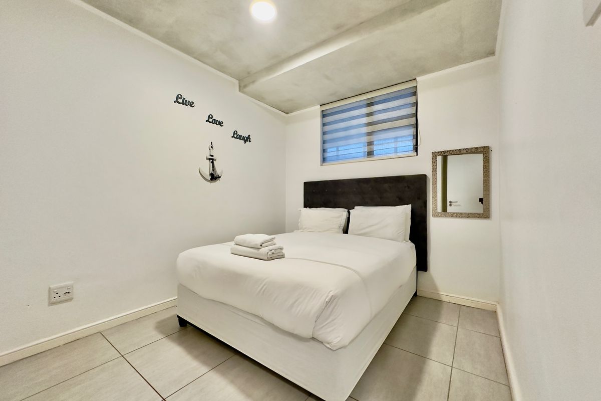 A compact bedroom featuring tiled flooring, a recessed ceiling design, and a window with a fitted roller blind.