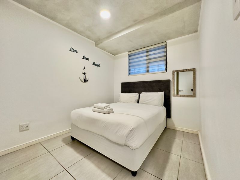 A compact bedroom featuring tiled flooring, a recessed ceiling design, and a window with a fitted roller blind.
