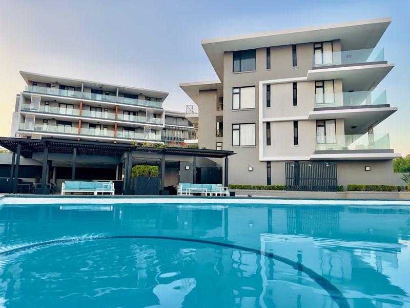 A modern apartment complex featuring a well-maintained swimming pool and a covered outdoor patio area with contemporary architectural design.