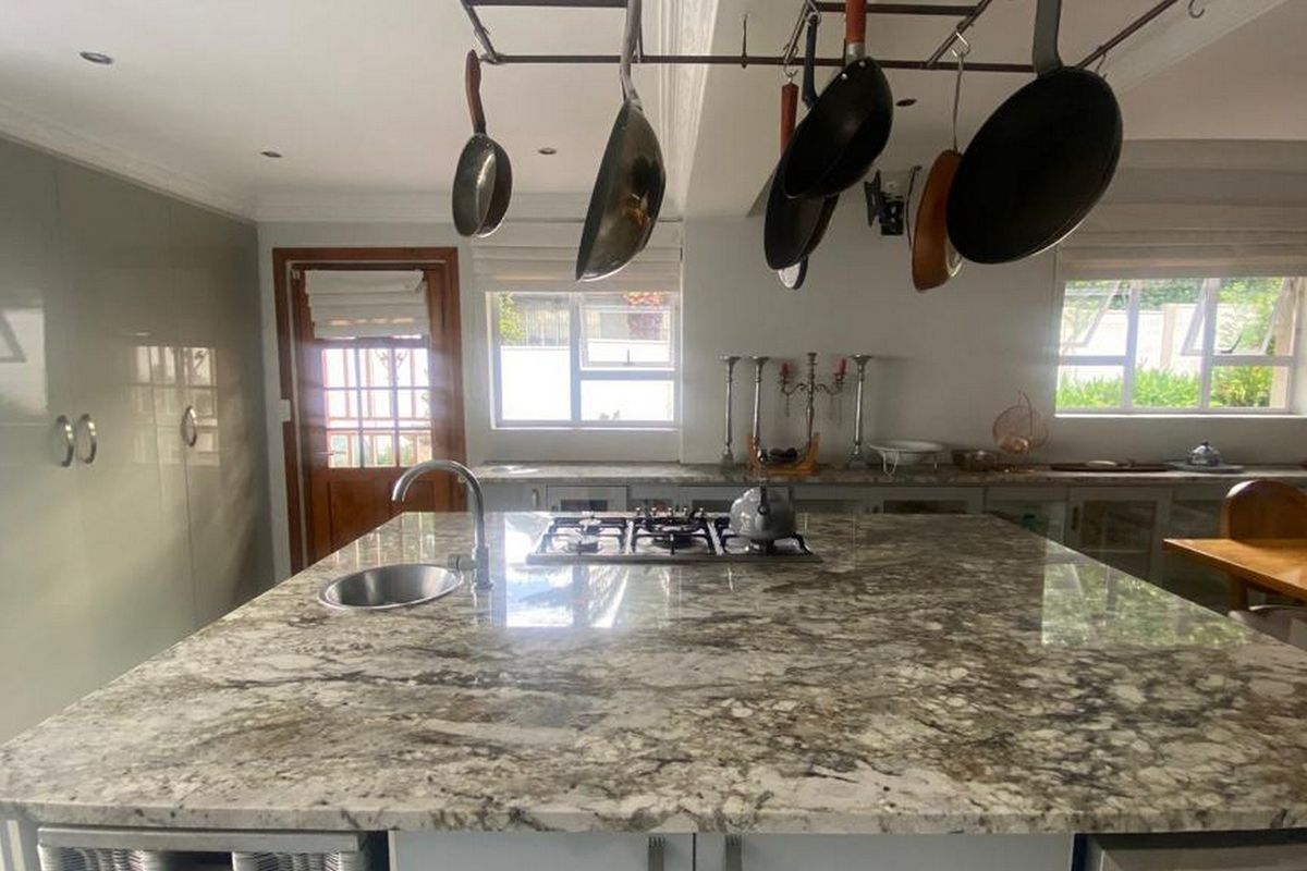 Spacious kitchen featuring a large granite island with a built-in gas hob, undermount sink, and overhead pot rack, complemented by ample built-in cabinetry.