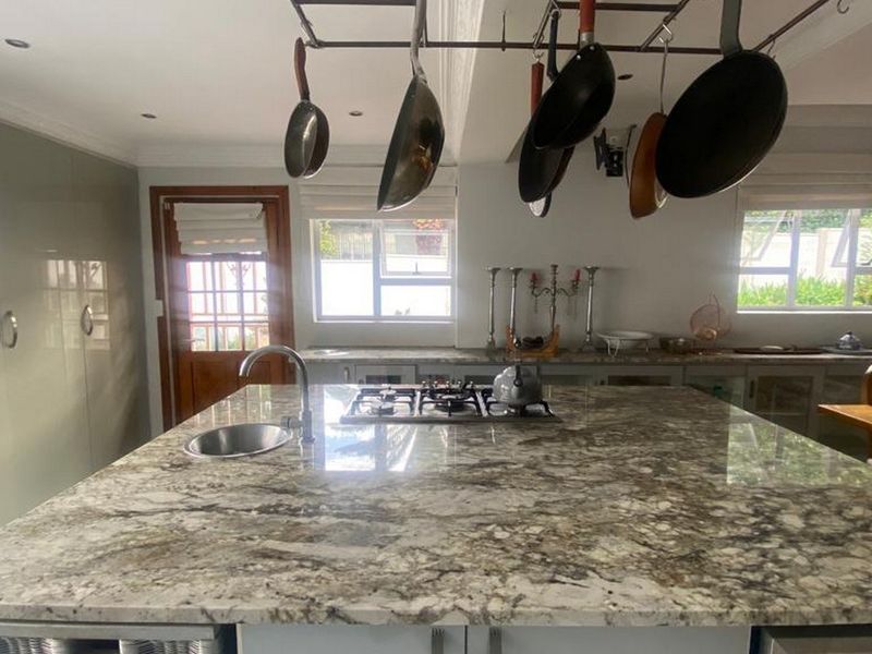 Spacious kitchen featuring a large granite island with a built-in gas hob, undermount sink, and overhead pot rack, complemented by ample built-in cabinetry.
