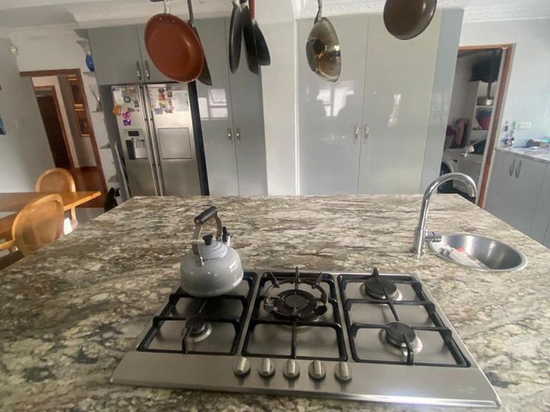 Modern kitchen featuring a large granite island with an integrated gas cooktop, prep sink, and ample built-in cabinetry for storage.