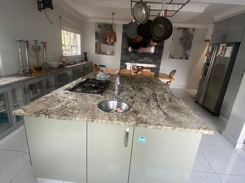 Spacious open-plan kitchen featuring a large central island with granite countertops, gas hob, integrated sink, and a cozy fireplace in the dining area.