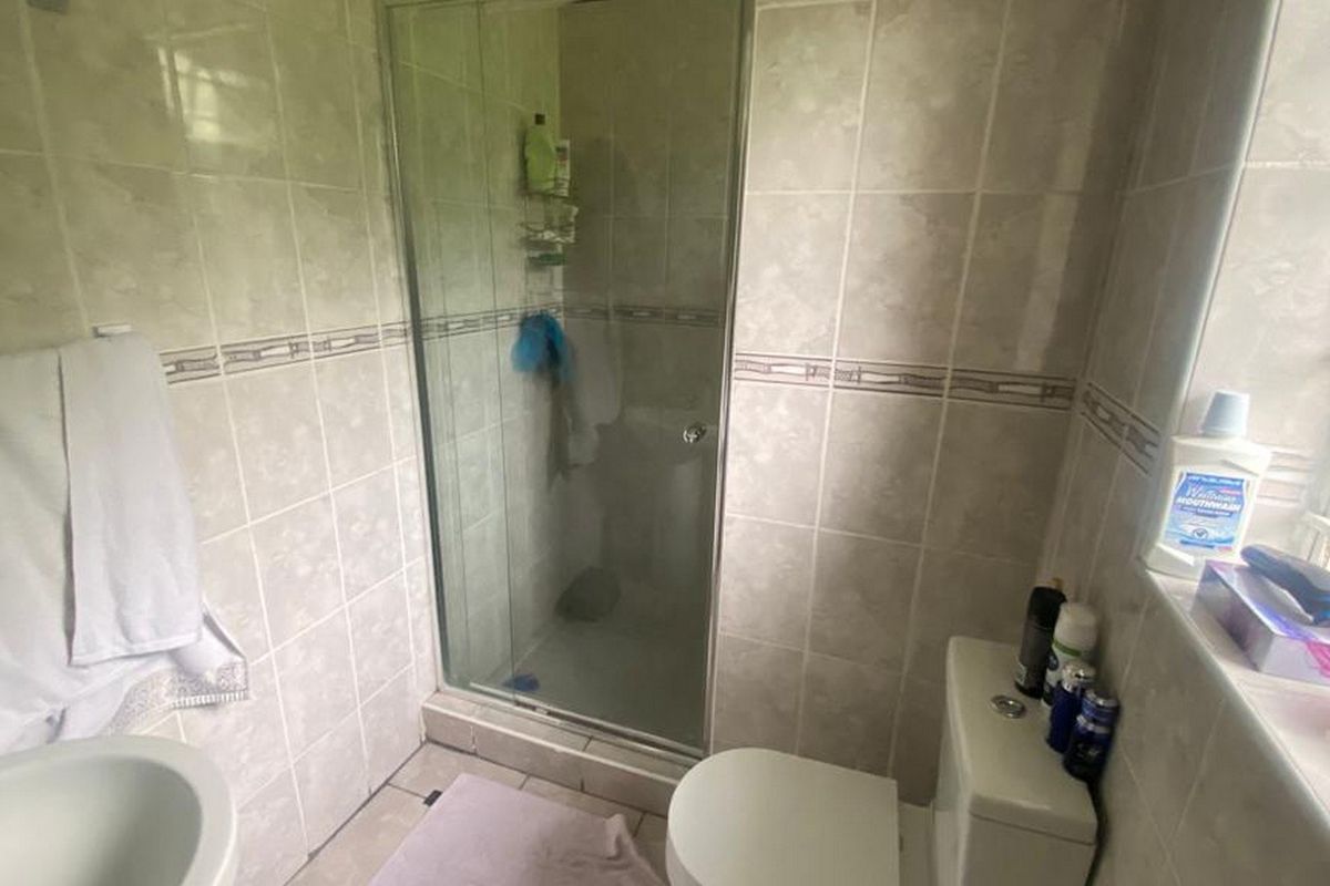 A functional bathroom featuring a glass-enclosed shower, pedestal basin, and toilet with neutral wall and floor tiling.