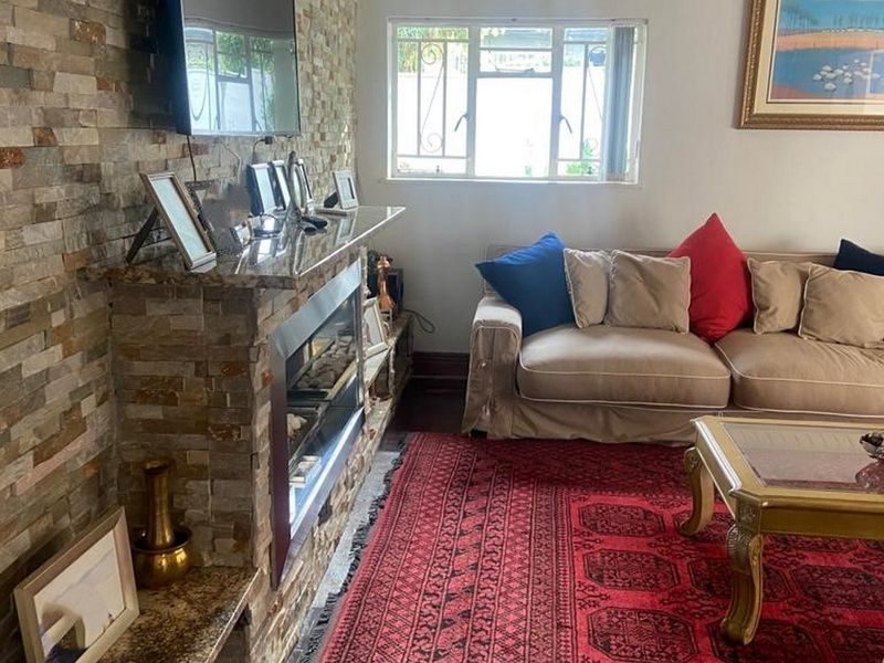 A cozy living room featuring a prominent stone-clad feature wall with a built-in fireplace and granite mantelpiece, complemented by natural light from the window.