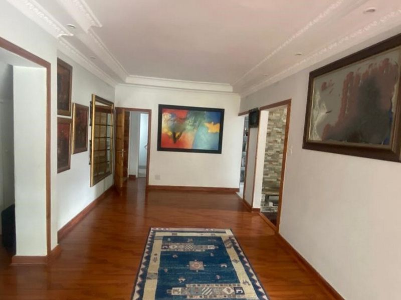 A spacious hallway featuring polished hardwood flooring, decorative crown molding, and recessed ceiling lighting, connecting multiple rooms throughout the home.