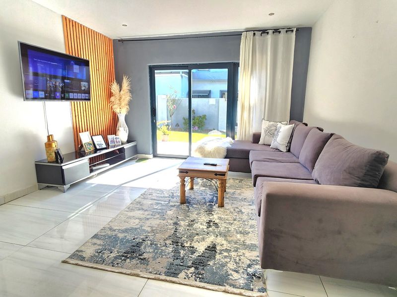 A bright living room featuring modern tiled flooring, a decorative wood slat feature wall, and large sliding glass doors providing access to the garden.
