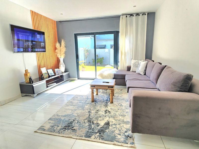A bright and modern living room featuring tiled flooring, a decorative wood-slat feature wall, and large sliding glass doors providing access to the rear garden.