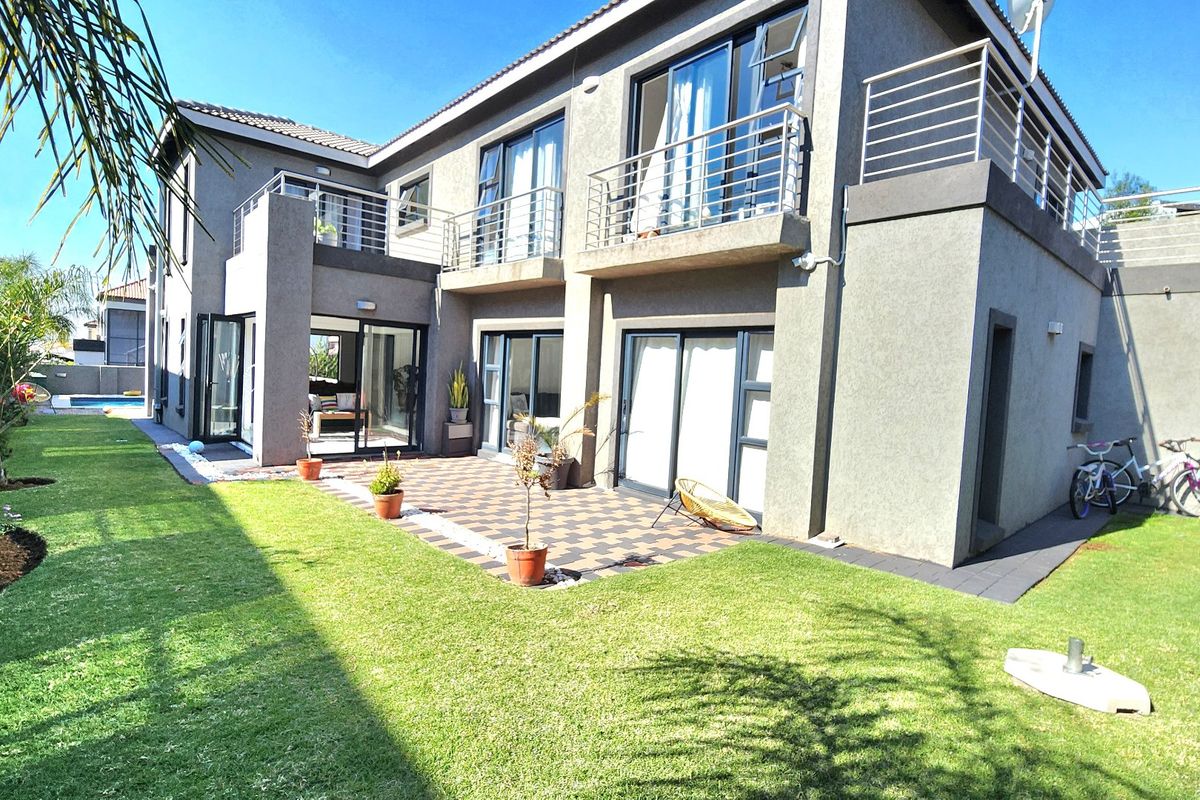 Rear view of a modern two-story house featuring a tiled patio, upper-level balconies with stainless steel railings, and a well-maintained garden lawn.