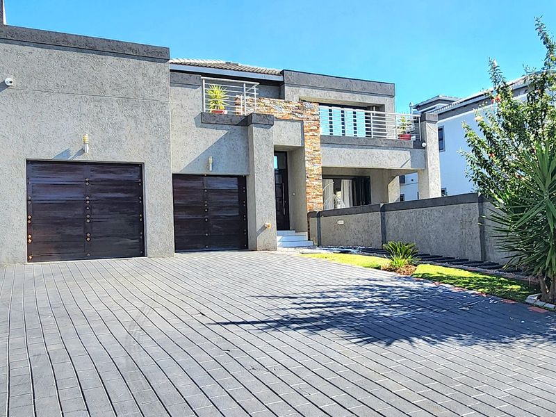 Modern double-story residence featuring a paved driveway, double garage, stone-clad accents, and an upper-level balcony with metal railings.