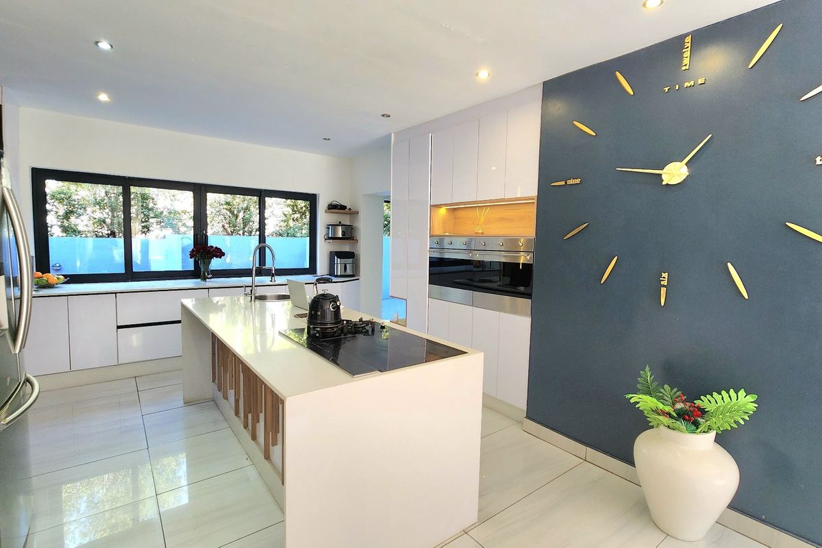 Modern kitchen featuring a central island with integrated cooktop, high-gloss cabinetry, built-in oven, and sleek stone countertops in a bright, open layout.