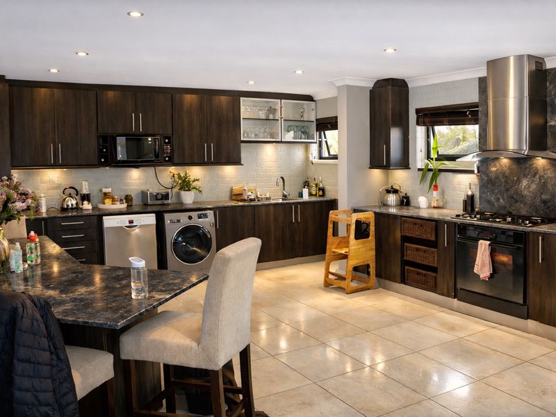 Modern kitchen featuring dark wood cabinetry, stone countertops, subway tile backsplash, and high-quality built-in stainless steel appliances with recessed lighting.