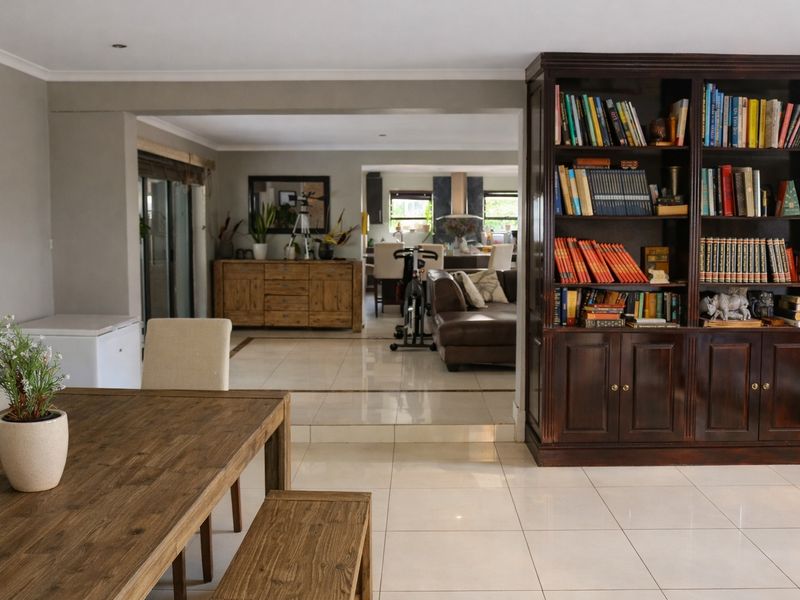 Spacious open-plan living area featuring large format floor tiles, recessed lighting, and a substantial built-in wooden bookshelf, creating a versatile and connected living space.
