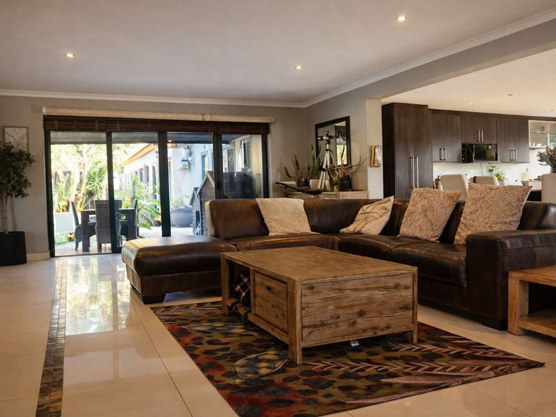Spacious open-plan living area featuring tiled floors, recessed lighting, and seamless flow to the outdoor patio, adjacent to a modern kitchen with built-in appliances.