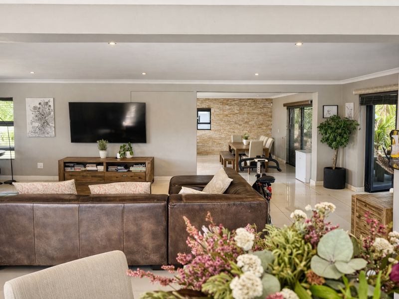 Spacious open-plan living and dining area featuring neutral tones, tiled flooring, recessed lighting, and a decorative stone feature wall.