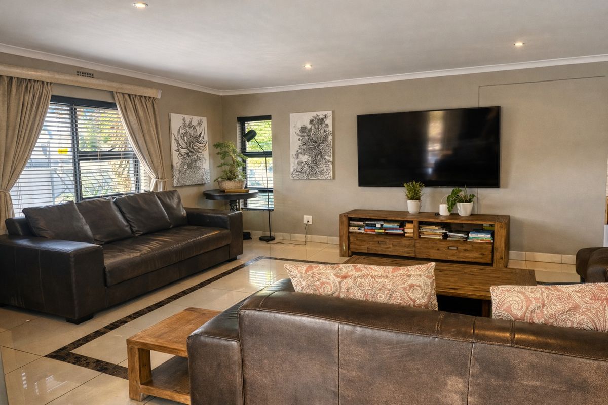 A well-maintained living room featuring neutral tiled flooring, recessed downlighting, and large windows with venetian blinds, creating a bright and comfortable living space.