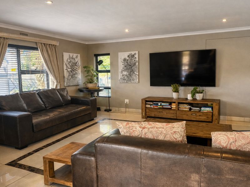 A well-maintained living room featuring neutral tiled flooring, recessed downlighting, and large windows with venetian blinds, creating a bright and comfortable living space.