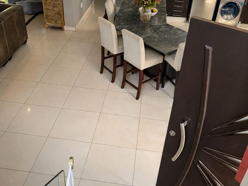 An open-plan living and kitchen area featuring modern tiled floors, a stone island, and integrated appliances, viewed from the staircase landing.
