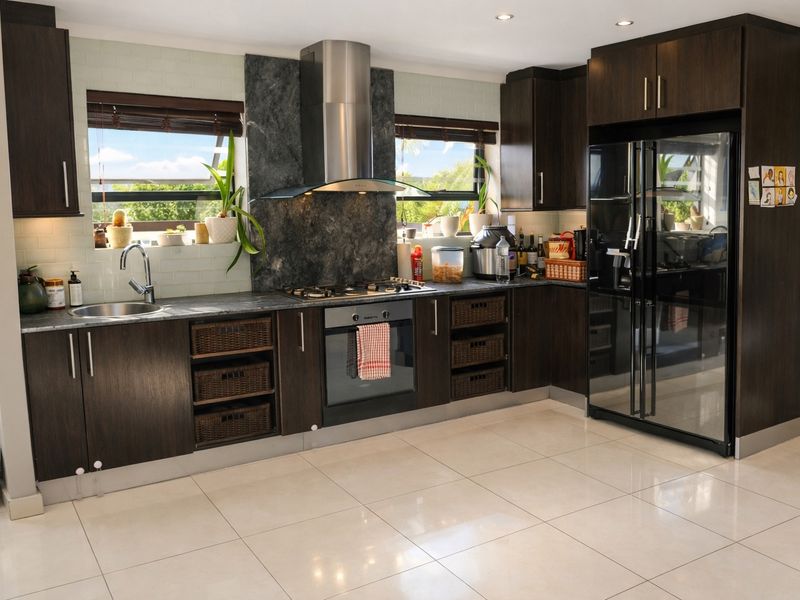 Modern kitchen featuring dark wood cabinetry, stone countertops, stainless steel appliances, and a tiled backsplash with ample natural light.