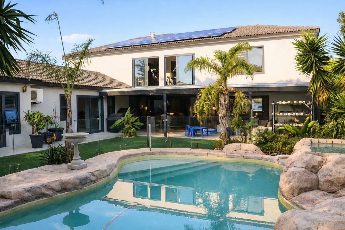 Rear view of the property featuring a swimming pool, landscaped garden, covered patio area, and solar panels installed on the tiled roof.