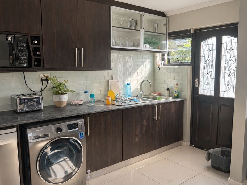 A functional kitchen featuring dark wood cabinetry, subway tile backsplash, integrated microwave, and direct access to the exterior via a decorative glass door.