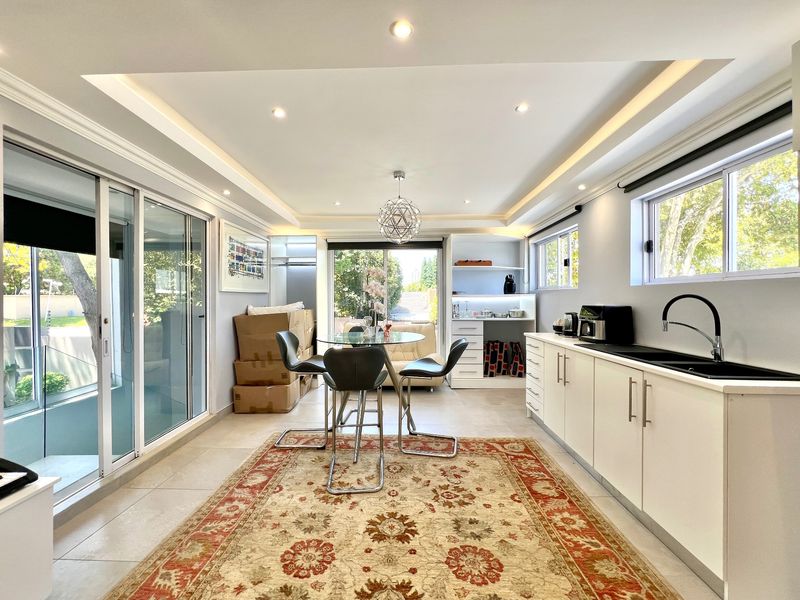 Modern open-plan living and kitchen area featuring sleek white cabinetry, black fixtures, recessed lighting, and large sliding glass doors leading to the exterior.
