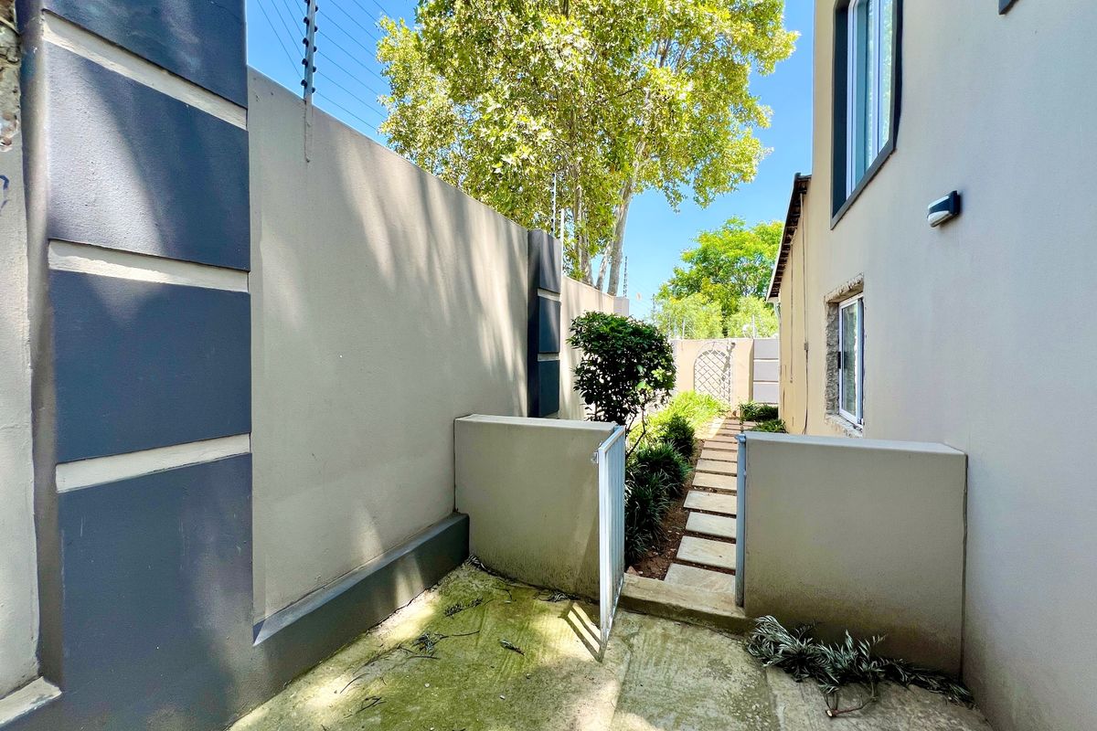 A side passage of the apartment featuring a paved walkway, boundary wall with electric fencing, and external lighting.