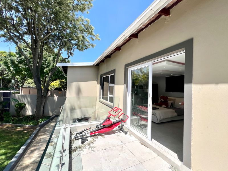 A modern balcony featuring a glass balustrade and tiled flooring, providing seamless indoor-outdoor flow to the adjacent bedroom through a large sliding glass door.